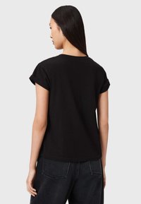 Tricou negru cu mâneci scurte și manșete rulate, confecționat din bumbac. Are o croială lejeră și un decolteu curat. Văzut din spate.