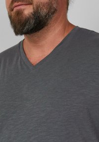 Szary t-shirt w kształcie V z miękkiej, teksturowanej tkaniny. Lekko wyblakły kolor, gładkie wykończenie i minimalistyczny design. Brak detali graficznych.