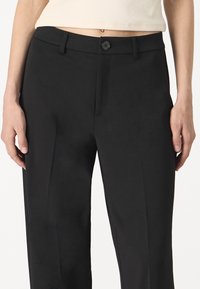 Black tailored trousers with a smooth texture, featuring a visible button closure, belt loops, and two front pockets.