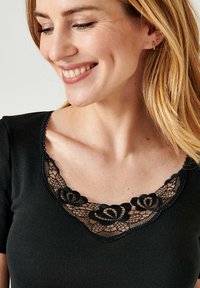 T-shirt nero con maniche corte, caratterizzato da un colletto in pizzo floreale nero. Il tessuto appare testurizzato e aderente con un colletto rotondo.