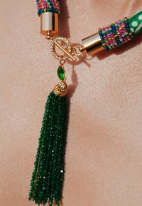 Collier à pampilles en perles vertes avec quincaillerie dorée, un fermoir étincelant et des perles texturées de couleurs vives. Les détails comprennent un accent en pierre précieuse verte.
