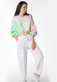Háčkovaná mikina s tie-dye vzorem v pastelových odstínech zelené, růžové a modré, kombinovaná s bílými tepláky se šňůrkou a bočními kapsami.