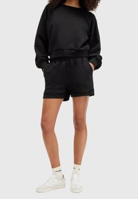 Czarna bluza z teksturowanymi rękawami raglanowymi, zestawiona z czarnymi szortami z siateczkowymi wykończeniami. Noszona z białymi trampkami i jasnymi skarpetkami.
