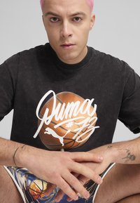 Sort, kortærmet t-shirt med et basketball-grafik og hvidt logo-design, parret med farverige shorts med et basketball-mønster.