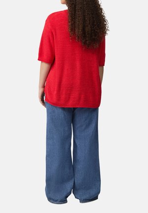 Rode gebreide trui met korte mouwen en een losse pasvorm, gecombineerd met wijde blauwe denim jeans. De textuur lijkt zacht en casual.