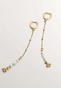 Pendientes de aro dorados con una cadena que presenta cuentas blancas y un pequeño colgante de hoja. El diseño incluye elementos lisos y texturizados.