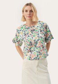 Bloemdruk top met puff mouwen, met een mix van roze, blauw, groen en zwarte tinten op een gestructureerde witte achtergrond.