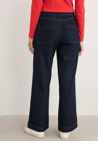 Breda jeans i mörk indigoblå med kontrastsöm. Har klassiska bakfickor och en slät, strukturerad yta. Enkel fåll.