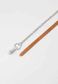 Cintura in pelle marrone con catena in metallo argentato. Include un anello tondo e un tirazip con incisione. Texture liscia e materiali a contrasto.