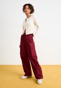 Ribbade krämfärgade koftan med en croppad design och framknappar, kombinerat med lösa maroon cargobyxor som har sidofickor och en logotyp.