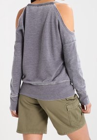 Haut gris à manches longues avec découpes aux épaules, doté d'un col et de poignets côtelés. Associé à un short cargo vert avec plusieurs poches.