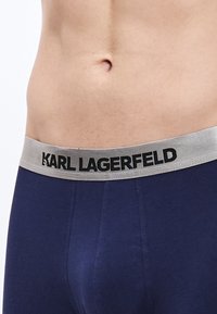 Boxer azul marino con una suave cinturilla gris que lleva un texto negro que dice "KARL LAGERFELD". Tejido liso y elástico.