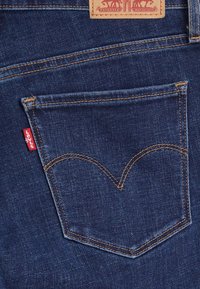 Rückansicht einer blauen Jeans mit orangefarbener Naht und einem braunen Lederpatch, das zwei Pferde und das rote Levi's-Label zeigt.