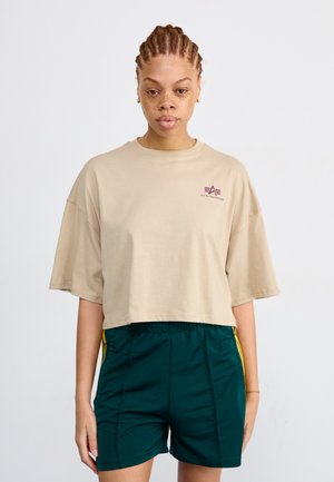 Bež cropped majica sa oversized rukavima i malim bordo logom, u kombinaciji sa zelenim šortsem koji ima žute bočne pruge i elastičnu struku.