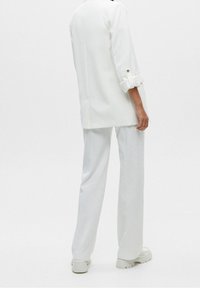 Blazer blanco de gran tamaño con mangas remangadas, combinado con pantalones blancos de pierna ancha. Tejido suave con un diseño limpio y minimalista.