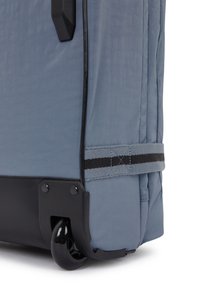 Blå tygresväska med en texturerad yta, svart plastbotten och hjul. Utformad med ett grått bälte med svarta sömmar som accent.