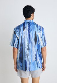 Short-sleeve shirt featuring a blue, abstract pattern with varying textures. Made from lightweight fabric, it has a relaxed fit and a pointed collar.