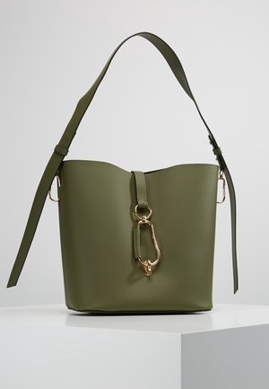 Sac seau en cuir vert olive avec bandoulière réglable et détail de fermoir en métal doré à l'avant, posé sur un piédestal blanc.