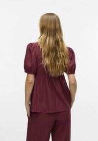 Haut bordeaux à manches bouffantes avec une coupe décontractée, texture côtelée et taille froncée ; associé à un pantalon assorti, vu de dos.