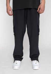 Pantaloni cargo neri con una vestibilità ampia, dotati di tasche laterali e una vita con cordoncino. Indossati con sneakers bianche.