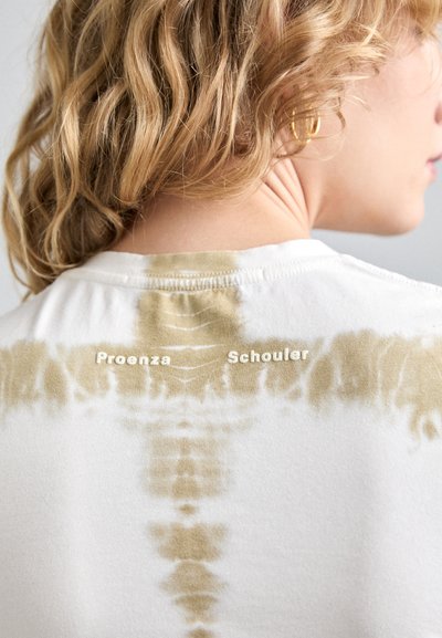 Hvit tie-dye t-skjorte med beige mønster. Har trykt "Proenza" og "Schouler" tekst på baksiden nær nakkekanten. Myk bomullsstruktur.