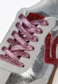 Zapatilla metálica plateada con cordones de purpurina rosa. Presenta acentos de ante, superficies brillantes texturizadas y un detalle de logo de purpurina roja.