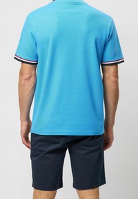 Jasnoniebieska koszulka polo o teksturowym wykończeniu, z paskowanymi mankietami w kolorze czerwonym, białym i granatowym. Dopasowana do ciemnogranatowych szortów.