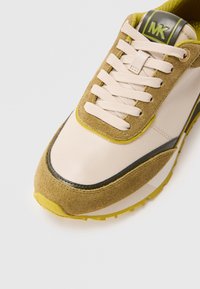 Beige leren sneaker met olijfgroene en gele suède accenten, gestructureerde veters en een afgeronde neus. Voorzien van een opvallend logo op de tong.
