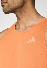 Πορτοκαλί αθλητικό τοπ χωρίς μανίκια με υφή υφάσματος και διακριτικό λογότυπο σε πιο ανοιχτή απόχρωση στην αριστερή πλευρά του στήθους.