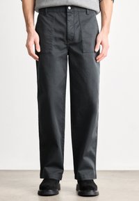 Sötétszürke, egyenes szárú nadrág elülső zsebekkel, gombos záródással és sima tapintású anyagból. Fekete lábbelivel viselve.