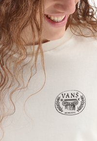 Cremefarbenes Sweatshirt mit einem runden schwarzen Logo, das den Text "VANS" und dekorative Lorbeerblätter zeigt, aus weichem Baumwollmaterial gefertigt.