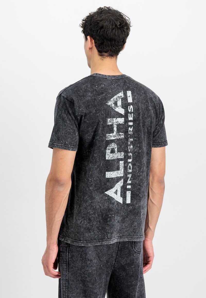 Tricou din bumbac negru, cu imprimeu mare alb "ALPHA INDUSTRIES" pe verticală pe spate. Design cu mâneci scurte și guler rotund.