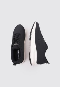 Zapatillas ligeras negras de material suave con suela blanca, que presentan cordones redondos, forro de malla y una pestaña en el talón.