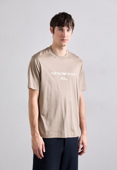 Beżowa koszulka z krótkim rękawem z miękkiej bawełny z klasycznym dekoltem. Posiada haftowane białe logo "Emporio Armani Milano" z przodu.