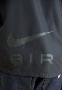 Bunda Nike Air v tmavě šedé látce, na zádech s velkým logem a nápisem "AIR" z reflexního materiálu. Hladká textura, volný střih.