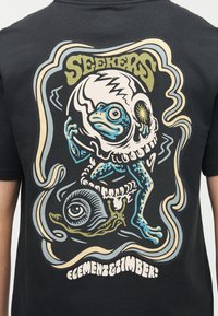 Στυλιζαρισμένος μπλε βάτραχος με κράνος κρανίο πατάει πάνω σε ένα σαλιγκάρι με μεγάλο μάτι, πλαισιωμένος από κυματιστές γραμμές, με τις λέξεις "SEEKERS" και "CEMENT TIMBER!".