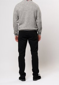 Grå stickad tröja med rund hals, i kombination med svarta byxor. Byxorna har bakfickor och är tillverkade av texturerat tyg. Svarta skor fulländar outfiten.