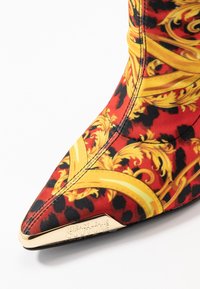 Stivale con stampa leopardata rossa e nera, decorato con un motivo barocco dorato, design a punta, tessuto testurizzato e logo in metallo dorato sul tallone.