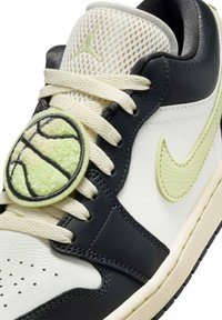 Skórzany niskoprofilowy sneaker w kolorach czarnym, białym i jasnym zielonym. Posiada siateczkowy język, teksturowaną gumową podeszwę oraz okrągłą naszywkę z motywem koszykówki na sznurowadłach.