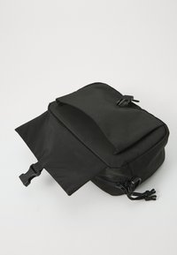 Svart stoffveske med glidelåsrom, med en fold-over topp og to snorstrammere for lukking. Glatt tekstur og minimalistisk design.
