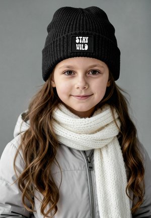 Black ribbed knit beanie with a "STAY WILD" patch; paired with a white textured scarf. The child is wearing a light gray coat.