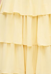 Miękki żółty materiał z warstwami falbanek tworzących stopniową teksturę i delikatne, opadające fałdy.