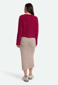Fuchsia Fuzzy-Strickpullover mit verkürztem Schnitt, kombiniert mit einem knielangen beigen Textilstiftrock und grauen Sneakern.