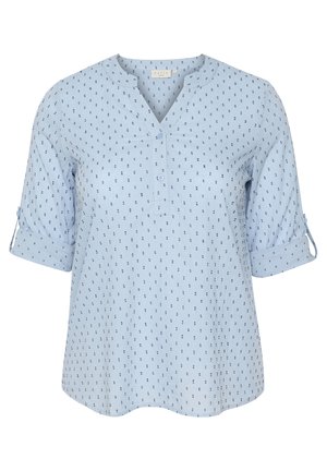 Blouse bleu clair avec un col rond, des manches courtes et un plastron de boutons. Présente de petits motifs à pois navy sur l'ensemble du tissu.