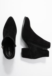 Botines de ante negro con punta afilada, tacón cuadrado y cierre lateral. Textura suave con un acabado mate. Nombre de la marca visible en el interior.