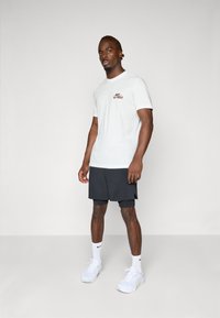 Hvid bomulds t-shirt med "Just Do It" logo, parret med mørke shorts. Tilbehør inkluderer hvide sneakers og ankelstrømper.