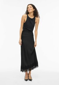 Črna obleka brez rokavov z oprijetim korzetom, tekočo krilo in čipkastim robom na spodnjem delu. Kombinirana s črnimi čevlji z visokimi petami.