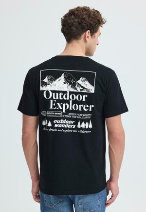 Man die een zwart T-shirt draagt met een ontwerp op de achterkant van een berggrafiek en de tekst "Outdoor Explorer" en "Outdoor wonders" in wit.