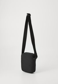Svart skulderveske laget av glatt stoff, firkantet form med glidelås, og justerbar stropp for enkelhet. Minimalistisk design.