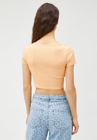 Kurzarmliges, geripptes, cropped Top aus hellem Orange, kombiniert mit hoch taillierten blauen Jeans mit floralem Muster.